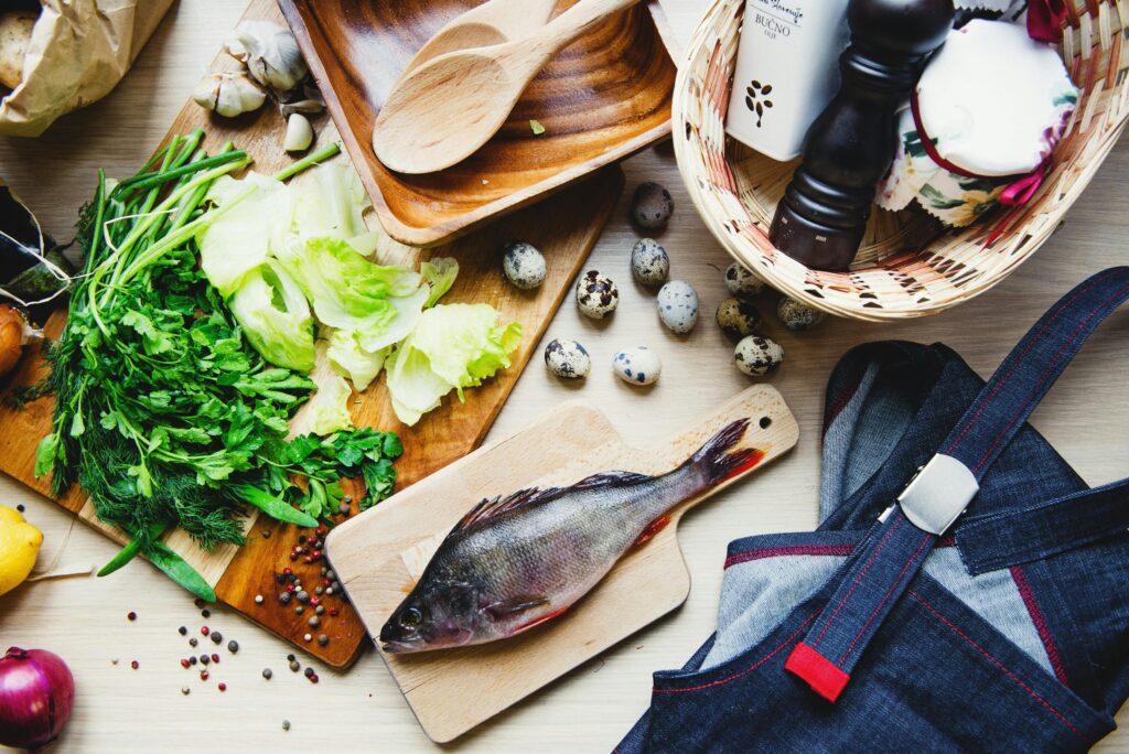 pexels-photo-3952052-3952052 Top view of fresh fish and vegetables put on cutting board near wooden dishware and wicker basket with pepper shaker and jar in kitchen